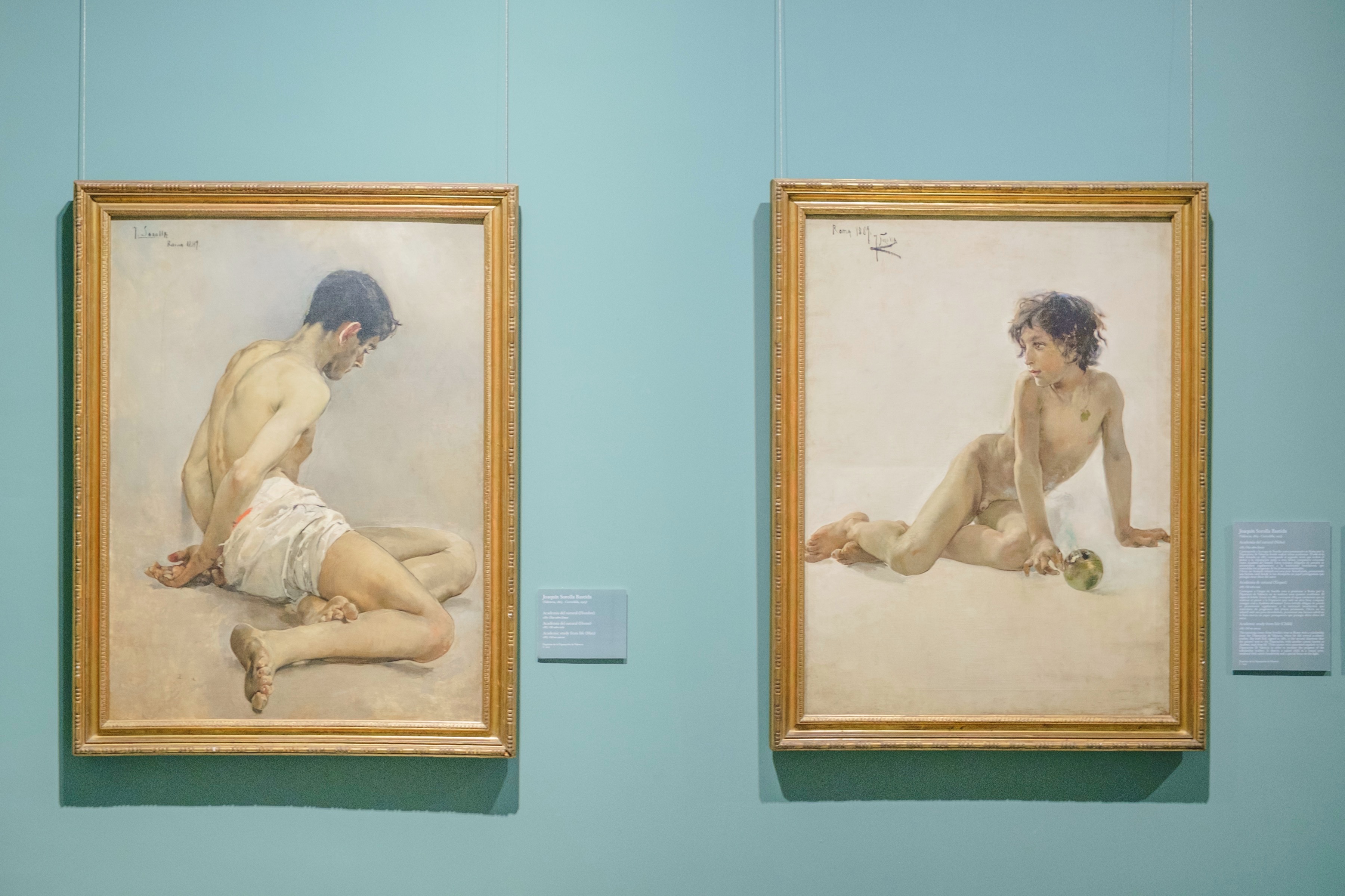 Pair of figure paintings displayed on a blue-green gallery wall